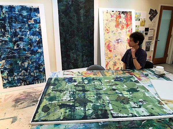 Artist Naomi Schlinke sits in her studio among her abstract paintings