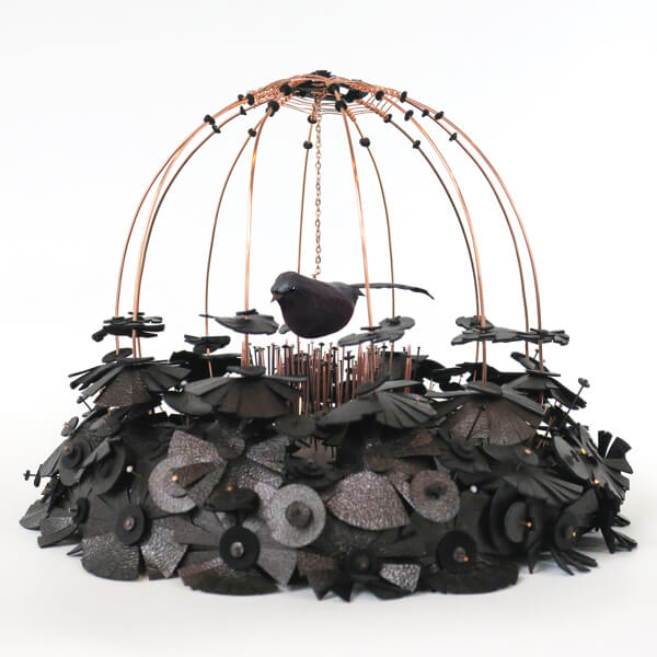 Photo of an artifical bird in a cage made of knitting needles and leather