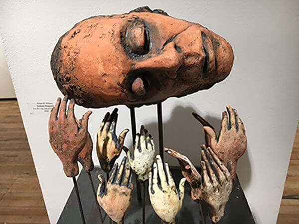 Clay sculpture of a human head on top of a collection of hands