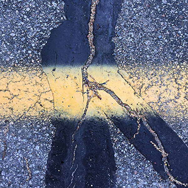 Photograph of a yellow line on the street, with cracks repaired by tar