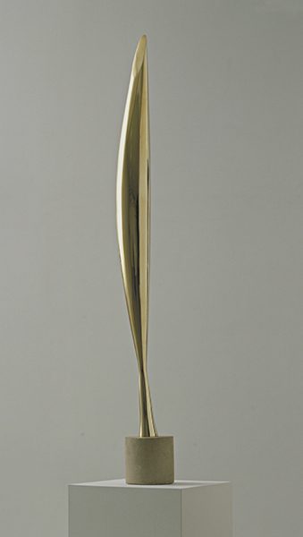 A tall, slim abstract bronze sculpture on a concrete pedestal