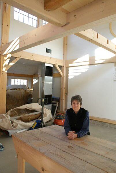 An artist sits at a table in her recently renovated studio, with white walls and wooden beams