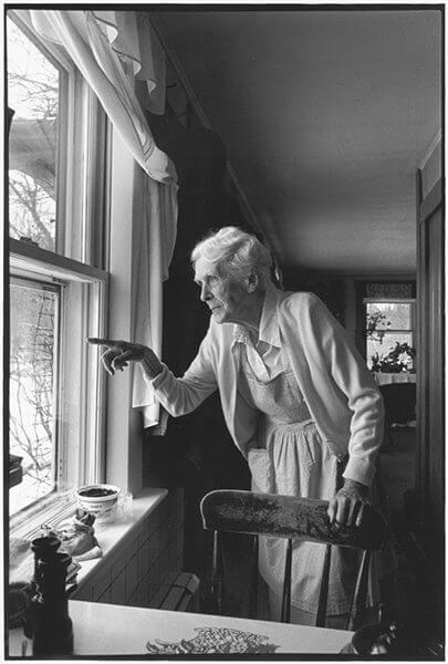 Black and white picture of an elderly woman pointing out a window