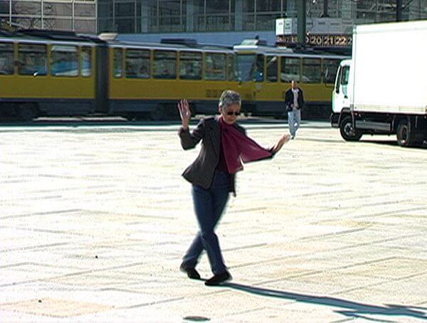 A shot from a video of a woman in a purple scarf dancing on an empty street square