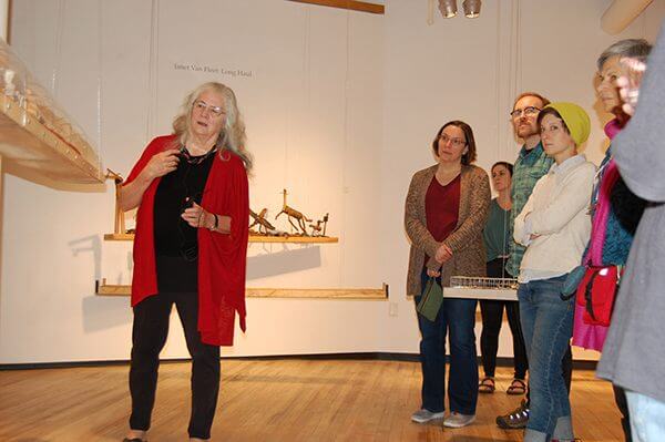 An artist at a gallery speaks to a crowd looking at her sculptures