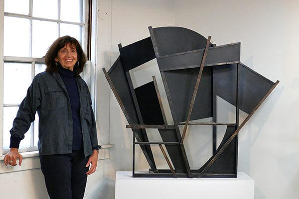 A sculptor in her studio next to a painted aluminum sculpture