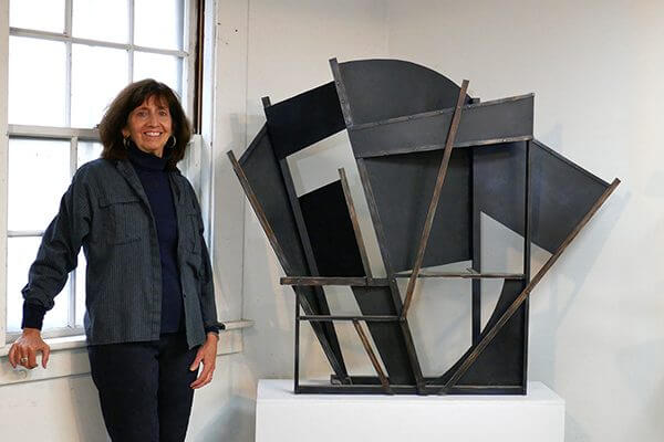 A sculptor in her studio next to a painted aluminum sculpture