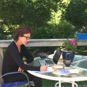 A woman working on a laptop and notepad on an outdoor deck