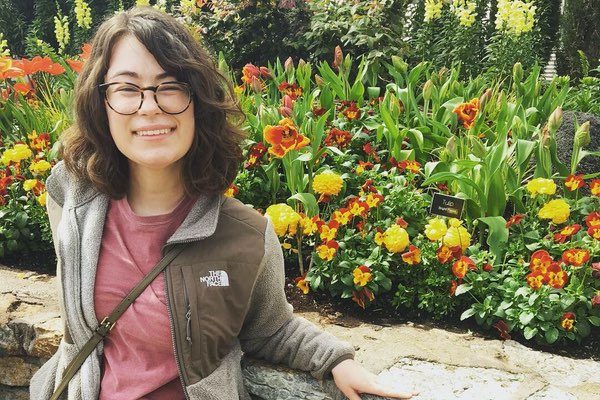 Image of writer Kayla Lutes in front of a flower bed