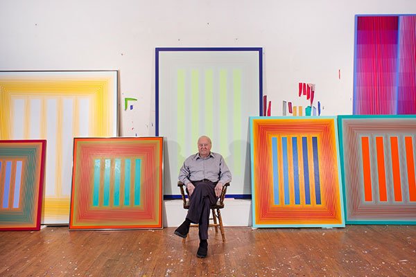 Portrait of an artist sitting in the studio surrounded by his paintings