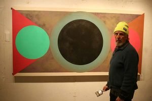 A painter stands in front of one of his geometric abstract works