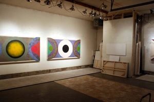 Geometric abstract paintings line the wall of Sandy Sokoloff’s studio