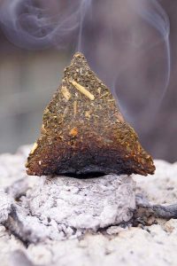 A triangle of compressed medicinal herbs smoking as part of an art installation