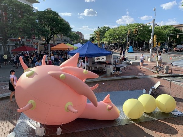 A large blow-up pink and yellow creature installed in a public square
