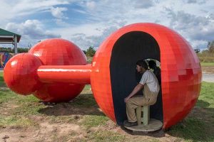 A red spherical sculpture in a park with people sitting inside one of the spheres
