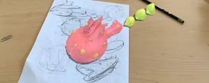 An AR visualation of a pink and yellow creature on a desktop