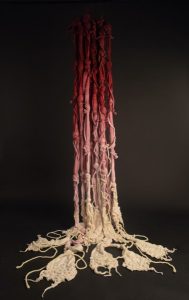 Long, thick pieces of red to white ombre fiber hang from the ceiling as an art installation
