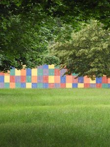 A photograph of a colorful wall behind grass and a tree
