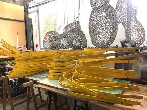 Yellow metal arches and webbed metal are works in progress in an artist's studio