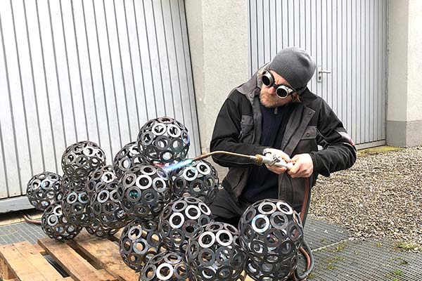 An artist uses a torch to work on a metal sculpture outside