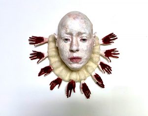 A wall sculpture of a woman's head wearing a collar of bloodied hands around her neck