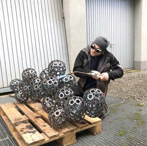 An artist uses a torch to work on a metal sculpture outside