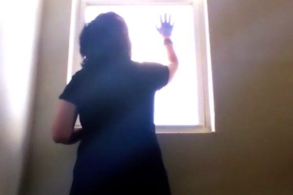 A woman wearing gloves looks out a bright window