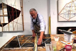 A painter uses a ruler to draw lines on a work in progress in his studio