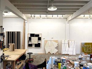 Works of art hang from the wall and lay against the wall of Hersh’s studio