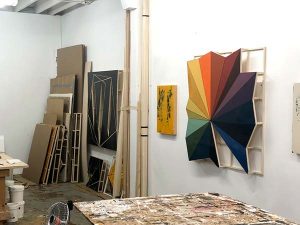 A wood-based work showing the spectrum of colors of the rainbow hangs from the wall of Hersh’s studio